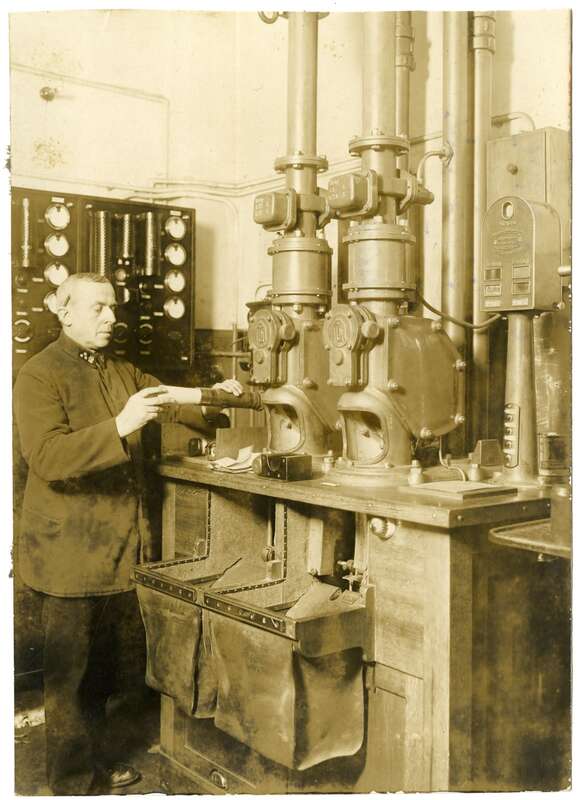Fotografie. Mitarbeiter der Deutschen Reichspost beim Verpacken einer Rohrpoststendung in eine Rohrpostbüchse vor einer Rohrpostanlage des Systems Mix und Genest
