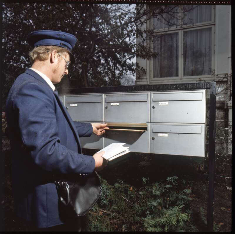 Fotografie / Diapositiv Zusteller der Deutschen Bundespost in Dienstkleidung bei der Zustellung von Briefsendungen über eine Hausbriefkastenanlage
