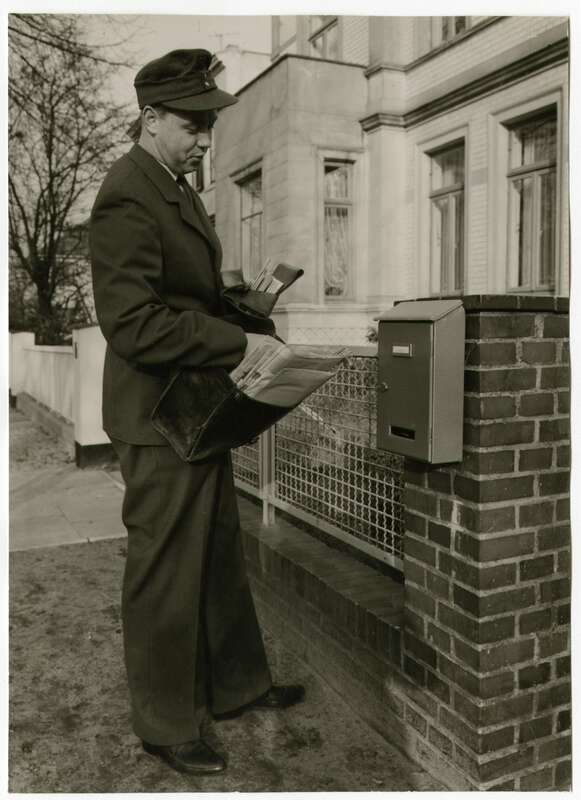Fotografie. Zusteller der Deutschen Bundespost in Dienstkleidung  bei der Zustellung von Briefsendungen über einen Hausbriefkasten in Hamburg