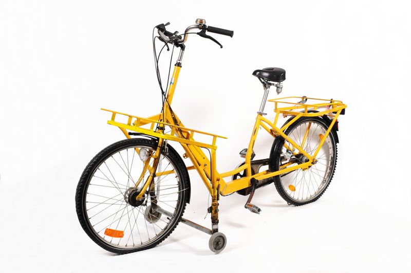 Fahrrad für Zusteller der Deutschen Post AG mit verlängertem Spezialrahmen, ausklappbaren Stützrädern und drei Gepäckträgern mit eingestellten Posttaschen